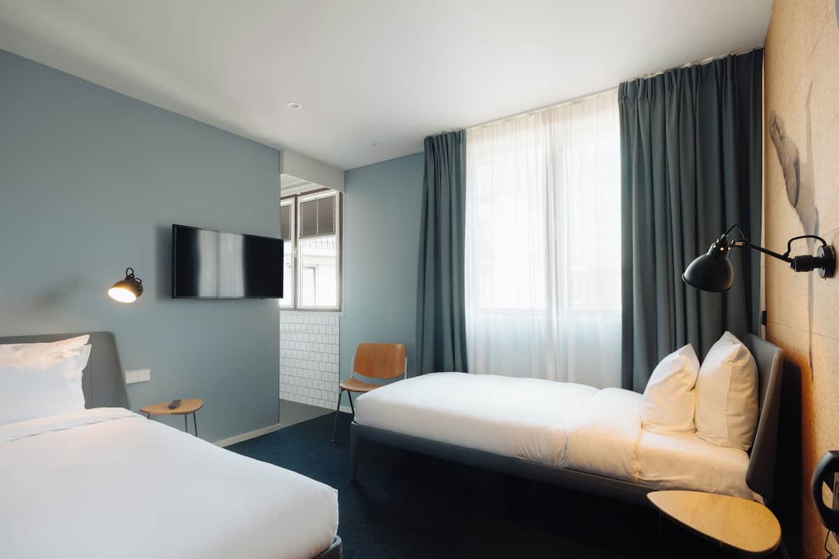 Quarto de hotel com duas camas, televisão, cadeira e escrivaninha.