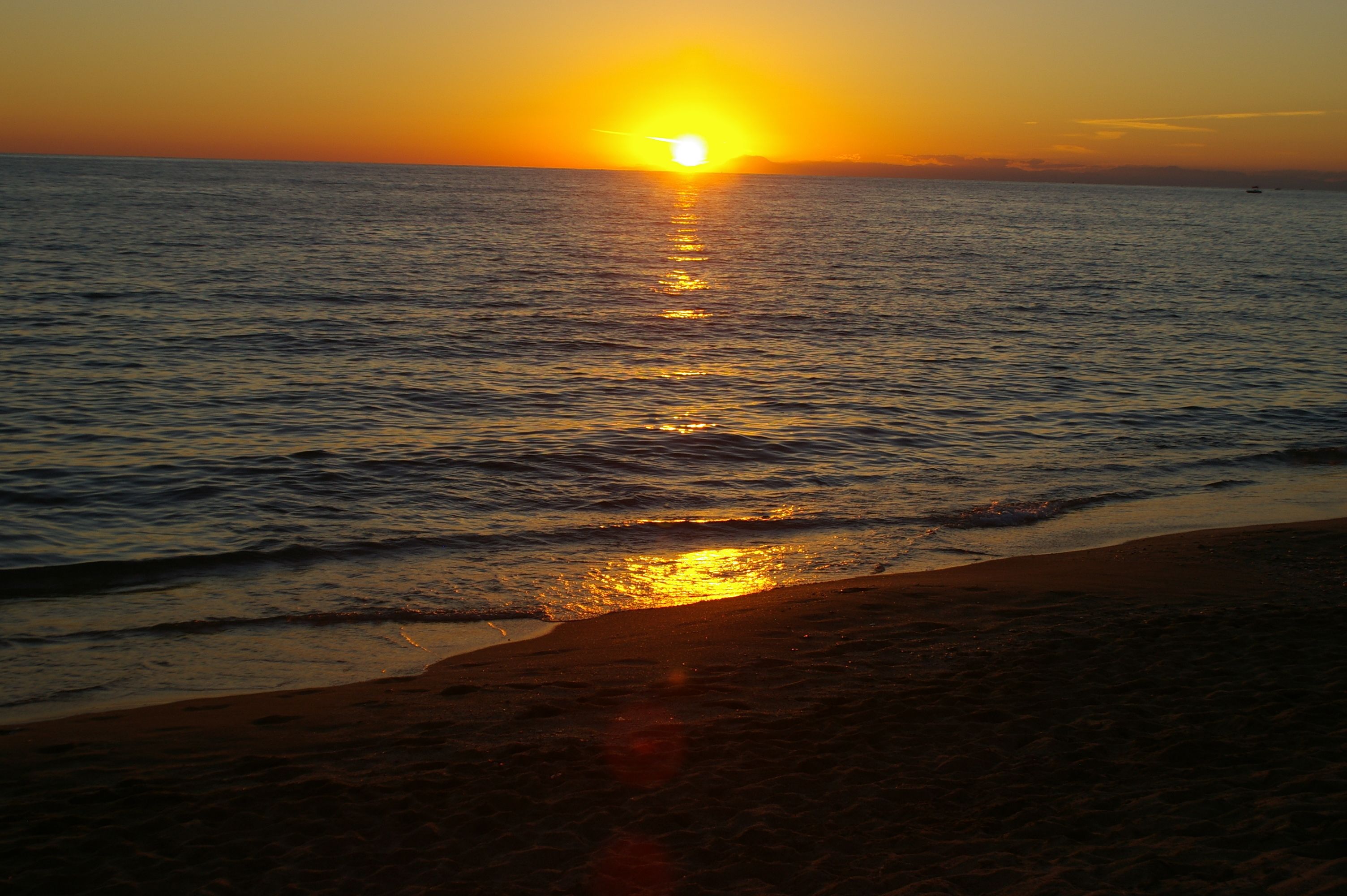 Um pôr do sol sobre uma praia, com águas calmas refletindo o sol.