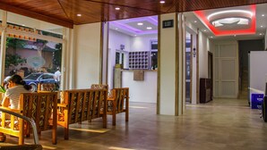 Zona de recepción con techo y paredes de madera, mostrador de recepción y área de estar con sillas estampadas.