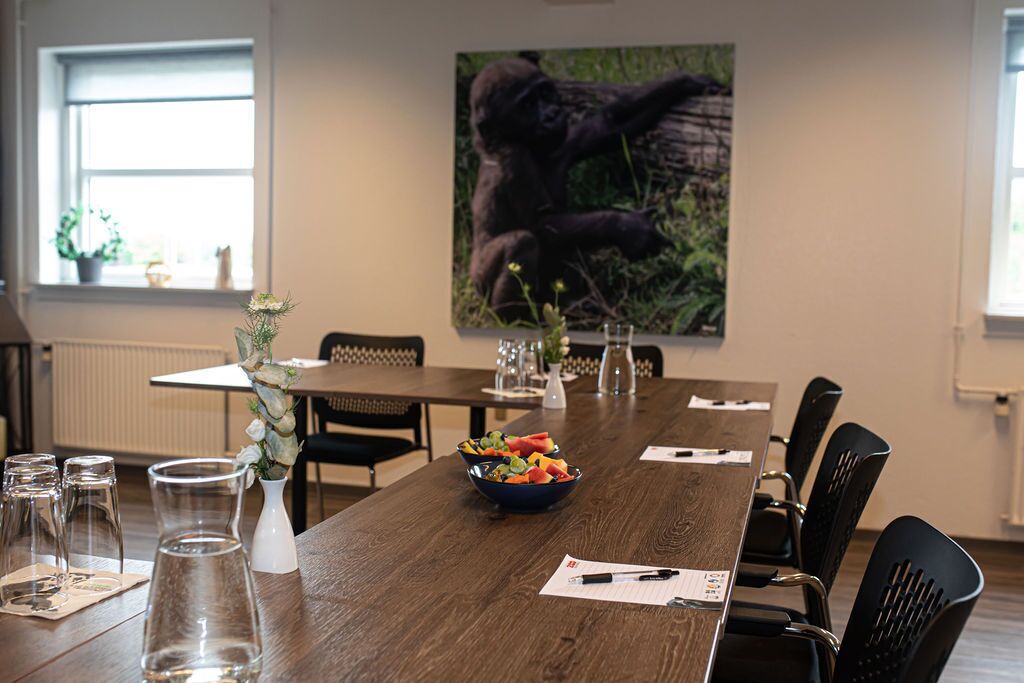 Un salón de conferencias con una larga mesa de madera, sillas negras, un frutero y un cuadro grande de un gorila en la pared.