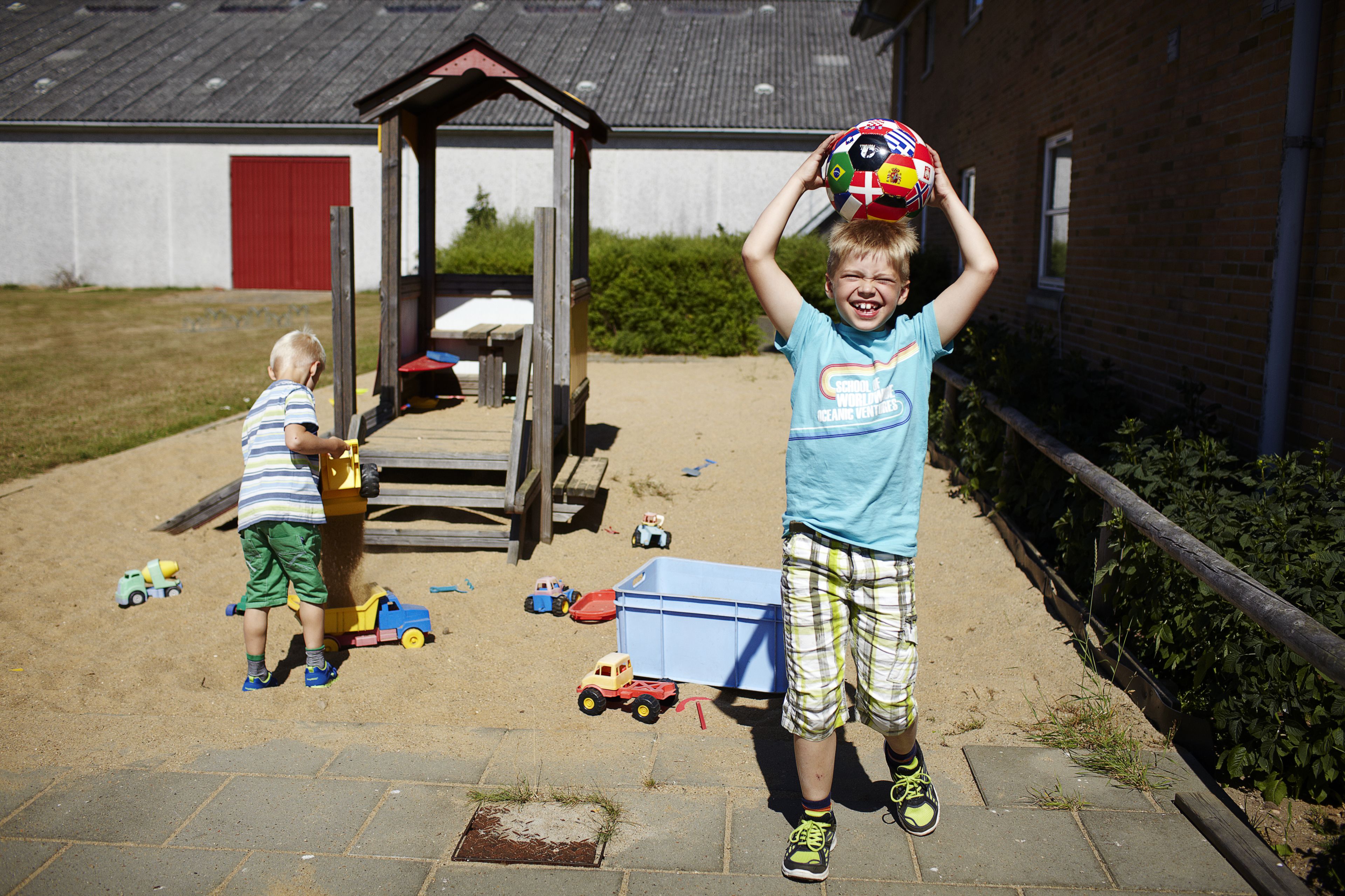 A child holding a soccer ball in a backyard with toys and a shed.