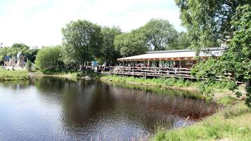 A riverside restaurant with outdoor seating overlooking a calm river, surrounded by lush greenery.