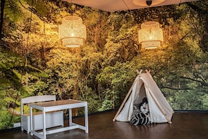 Um quarto com uma tenda, uma mesa e um mural na parede com tema de floresta.