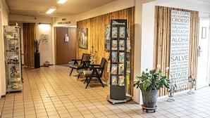 Zona de recepción con pared de madera, mostrador, sillas, una planta y un cartel con varios idiomas.