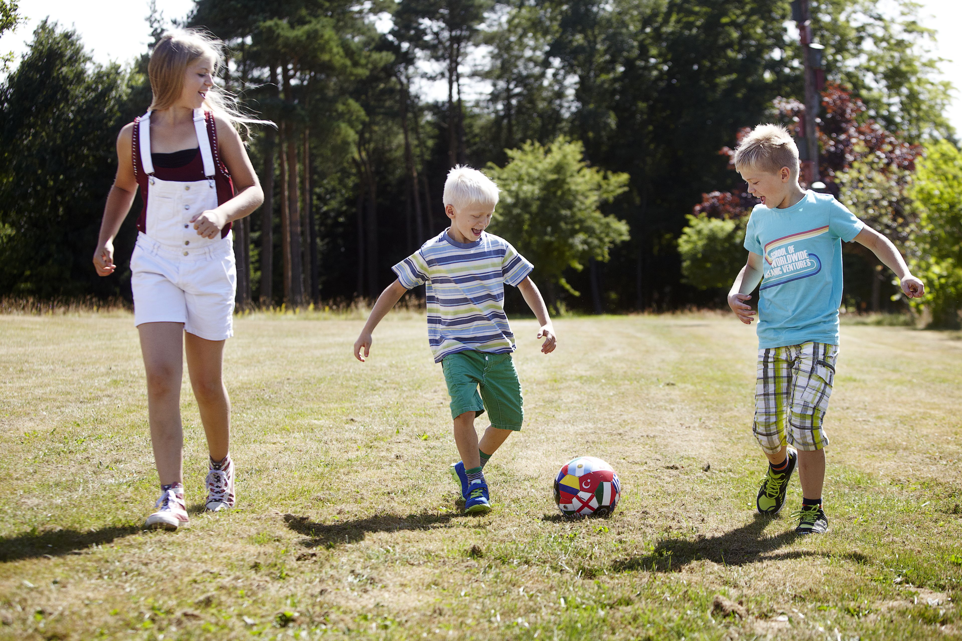 Three children playing with a soccer ball in a grassy field.