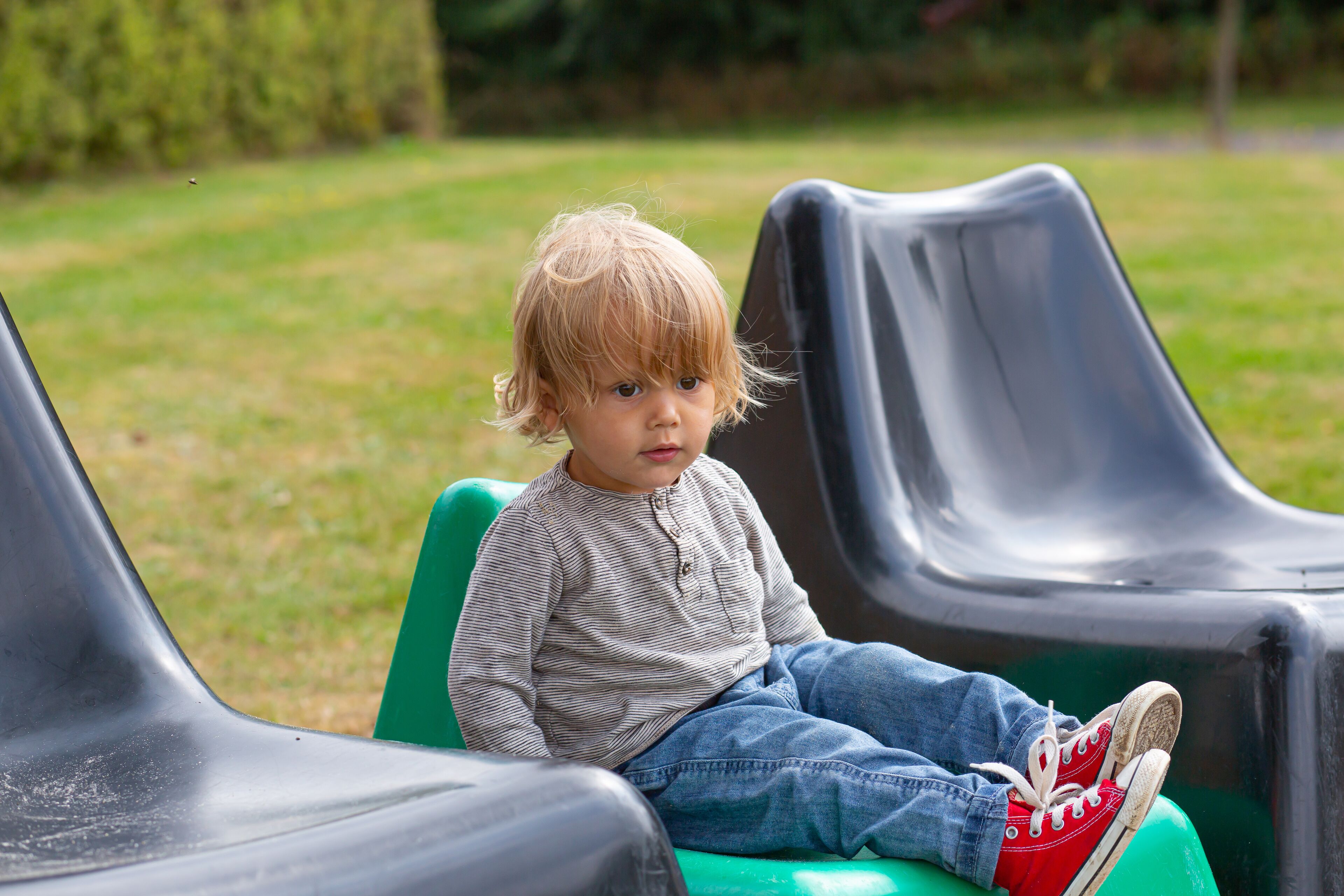 A child sitting on a green slide in a park.