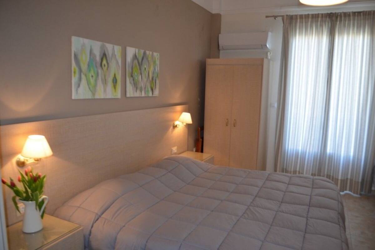 A hotel room with a bed, two wall-mounted lamps, a nightstand with a vase of flowers, and a wardrobe.