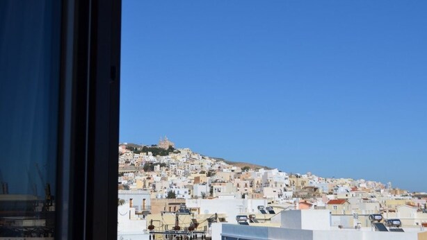 Un paysage urbain côtier avec un bâtiment imposant situé sur une colline, qui semble être un site historique ou religieux, ainsi que des bâtiments densément regroupés dotés d’une architecture caractérisée par des toits plats.