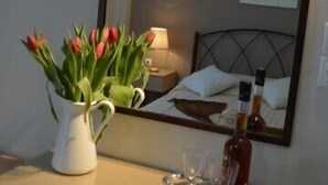 Une chambre d’hôtel avec un lit, une table de chevet ornée d’un vase de tulipes, une bouteille et un miroir qui reflète la pièce.
