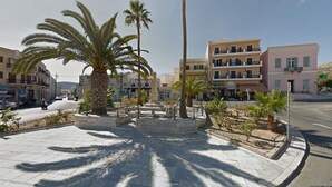 Une place publique bordée de palmiers, avec une statue et des bâtiments en arrière-plan.