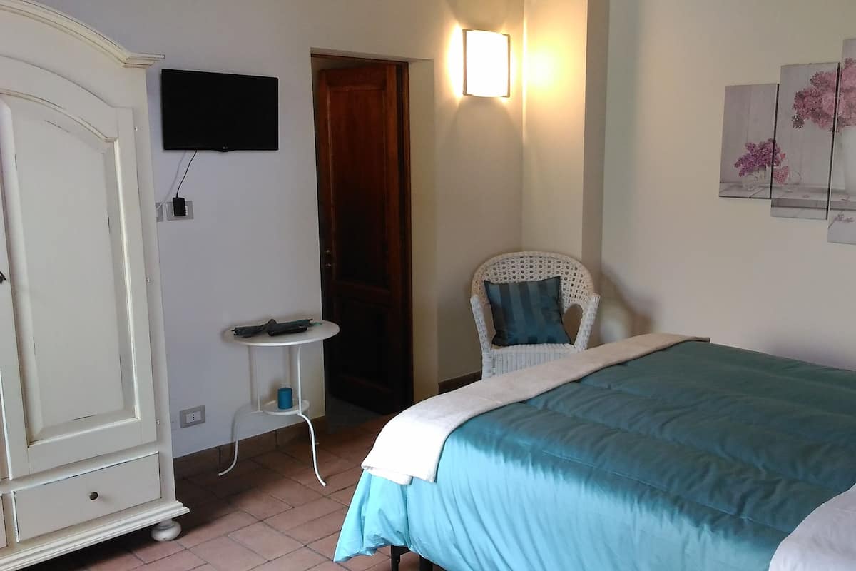 A bedroom with a bed, a chair, a wardrobe, a TV, and wall art.
