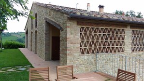 A stone building with a tiled roof, a lattice window, and a paved patio with wooden chairs. - Capanna 1826 (San Gimignano)