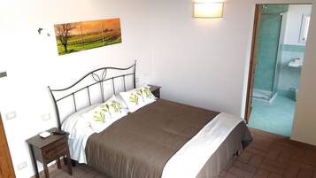 A single bed with a metal frame, a bedside table, and a nightstand. There is a wall-mounted light fixture above the bed and a painting above the nightstand.
