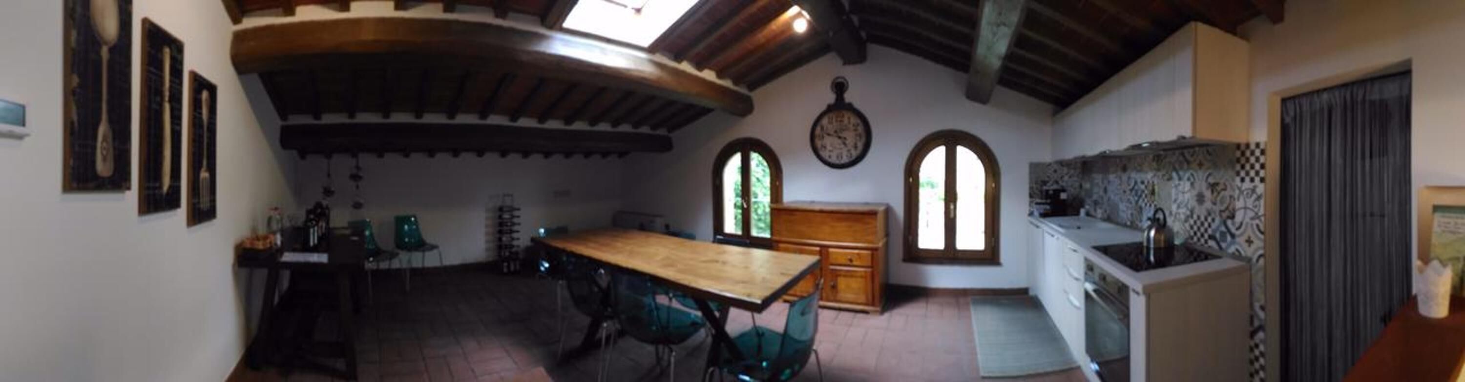 Een keuken met een houten tafel, stoelen, een klok en een raam.