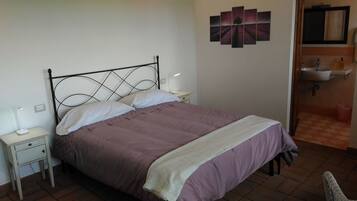 A single bed with a headboard, two bedside tables, a wall-mounted artwork, and a bathroom with a sink and mirror.