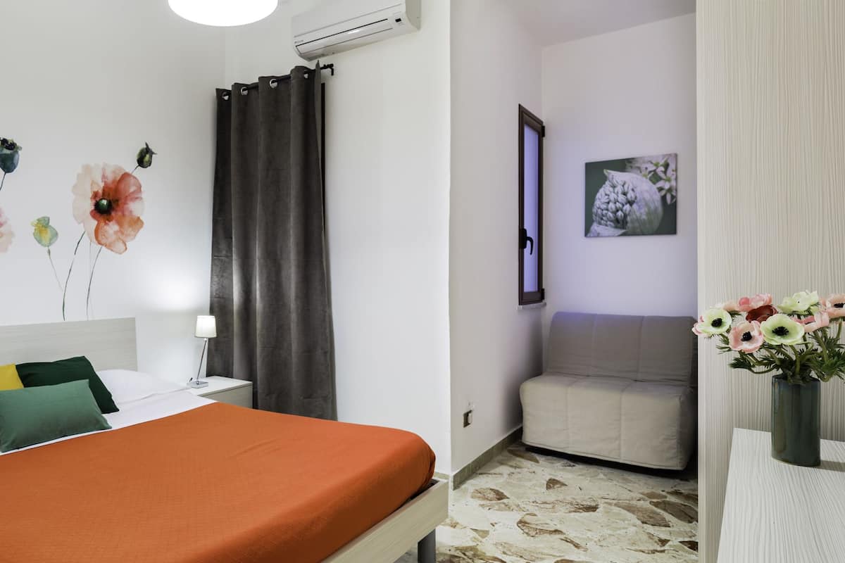 Ein Hotelzimmer mit Bett, Nachttisch, Lampe, Blumen in einer Vase und einem Gemälde an der Wand.