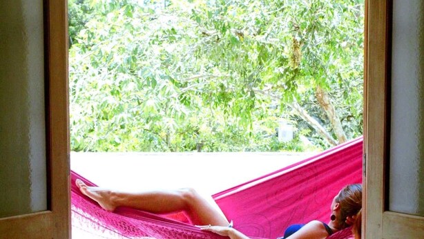 A person lying on a hammock in a doorway. - Casa Bacarirá (São Sebastião)