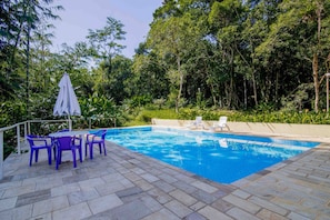 Piscina com deck revestido, rodeada por vegetação exuberante e árvores.