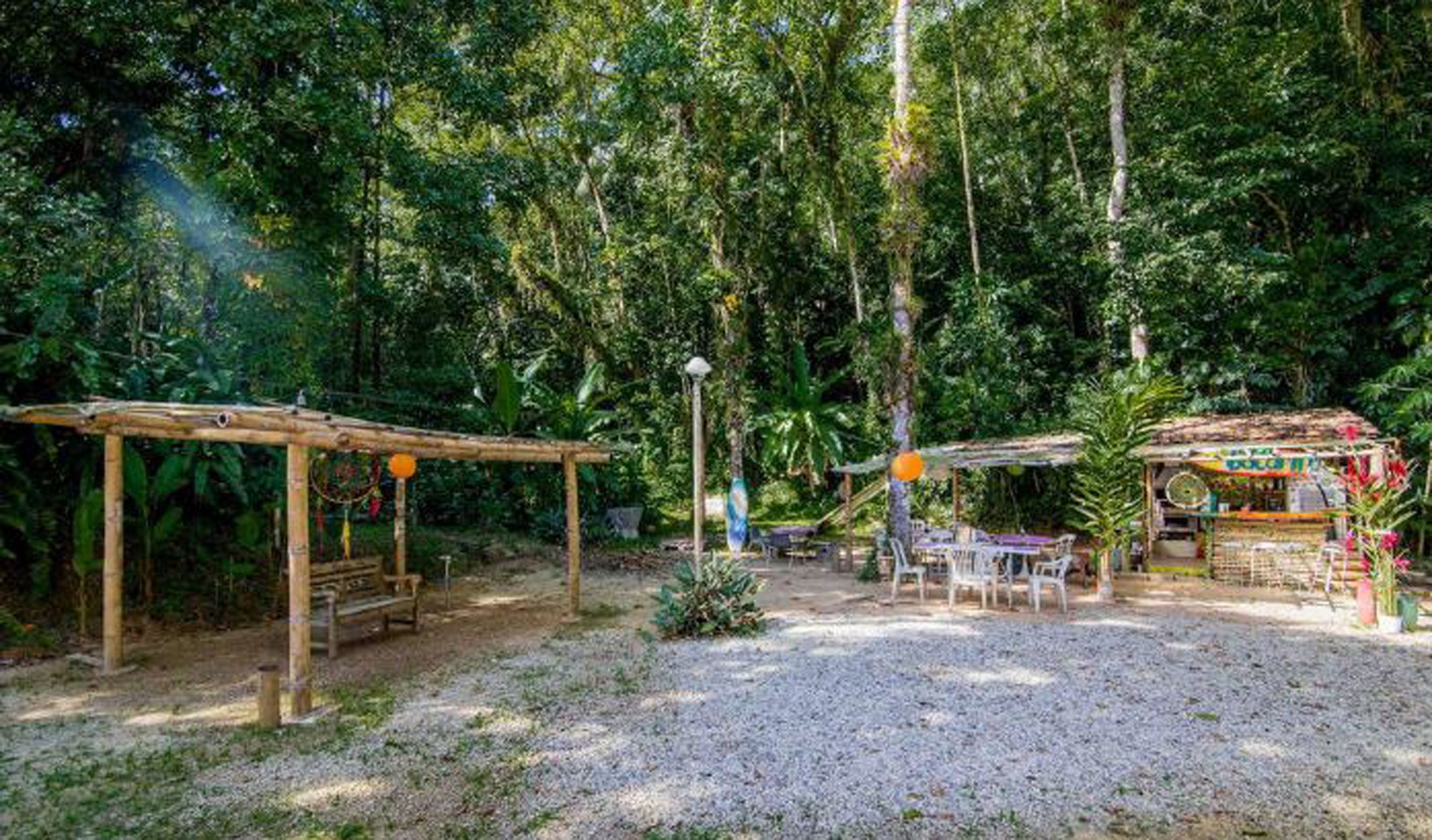 A rustic outdoor seating area with wooden structures and tables, surrounded by dense greenery.