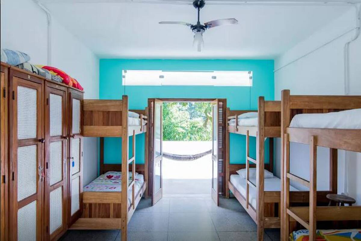 A dormitory room with bunk beds, a ceiling fan, and a view of greenery outside.