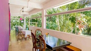 A dining area with large windows, ceiling fans, and wooden chairs. - Casa Bacarirá (São Sebastião)