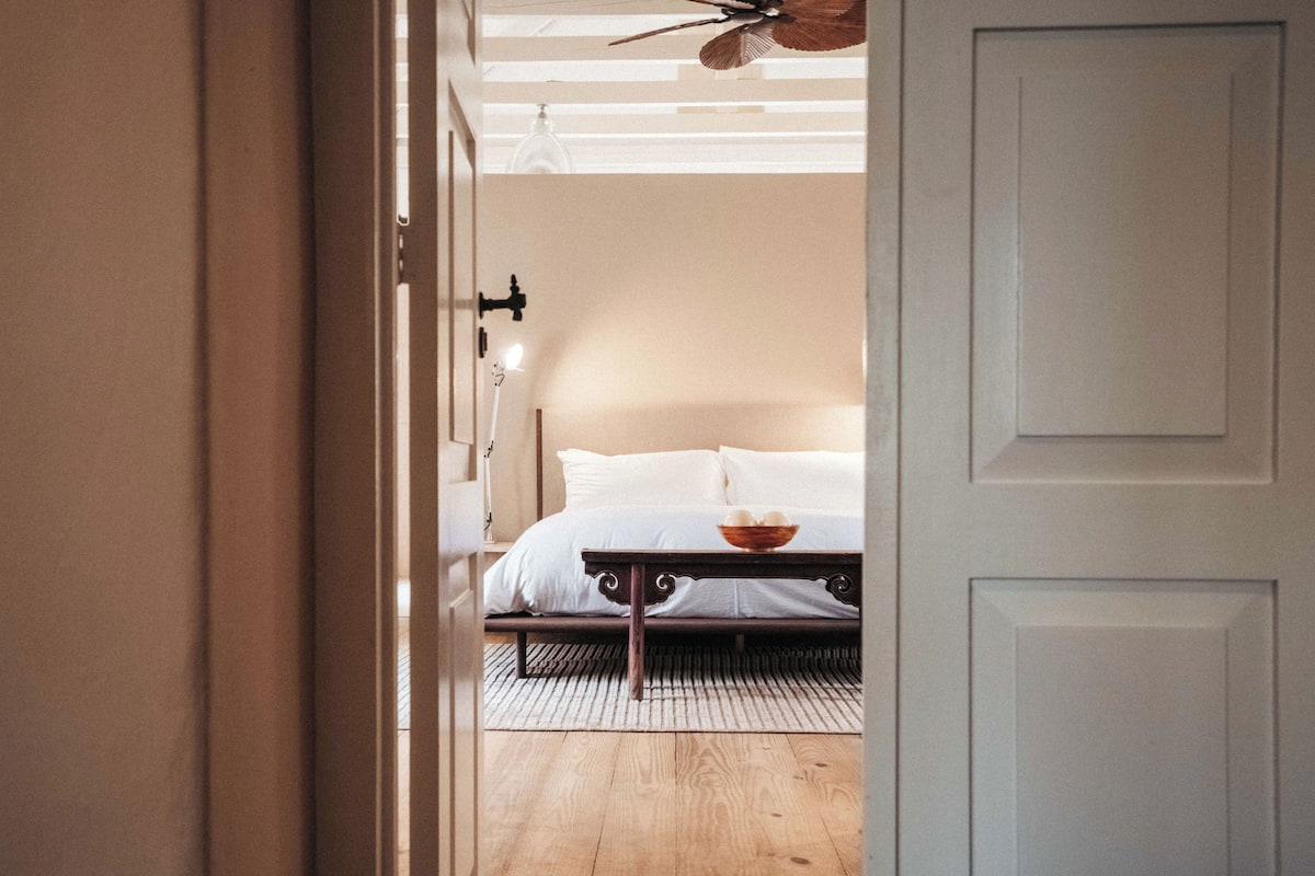 A bedroom with a bed, a bedside table, a ceiling fan, and a door.
