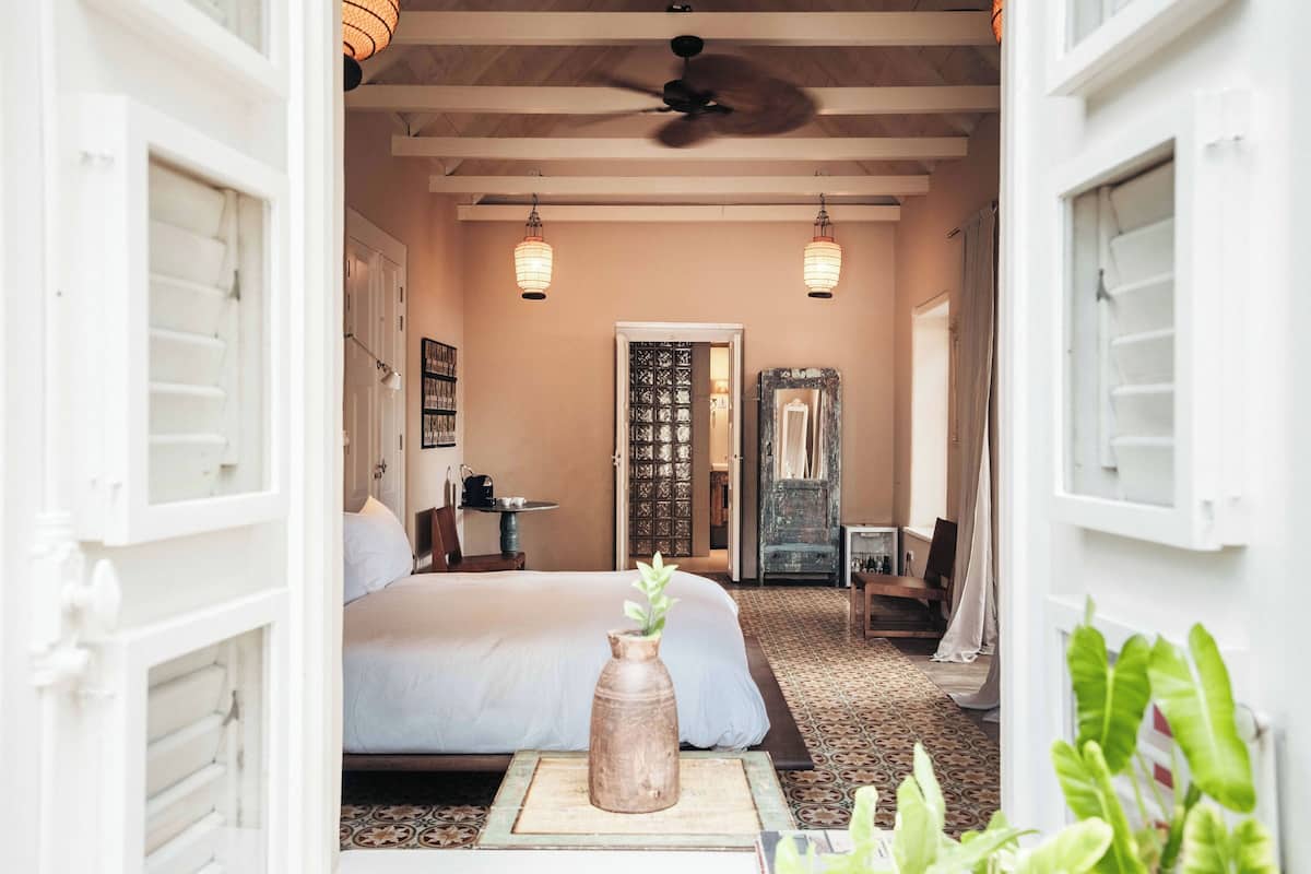 A bedroom with a bed, a wooden vase with a plant, a ceiling fan, and two hanging lanterns.