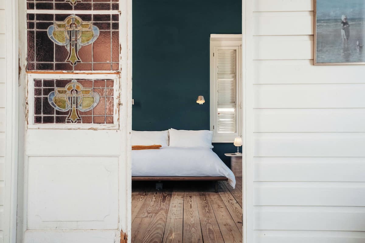 A bedroom with a wooden floor, white bed, and a door with stained glass.