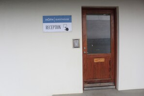 Una puerta de madera con un panel de vidrio y un cartel encima que dice "HÖFN GUESTHOUSE RECEPTION" con un icono de mano señalando.