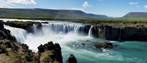 Una cascada se precipita sobre terreno rocoso bajo un cielo despejado.