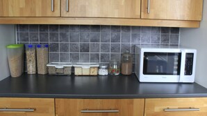 A kitchen with wooden cabinets, a tiled backsplash, and a microwave on the counter. - Höfn guesthouse (Höfn)