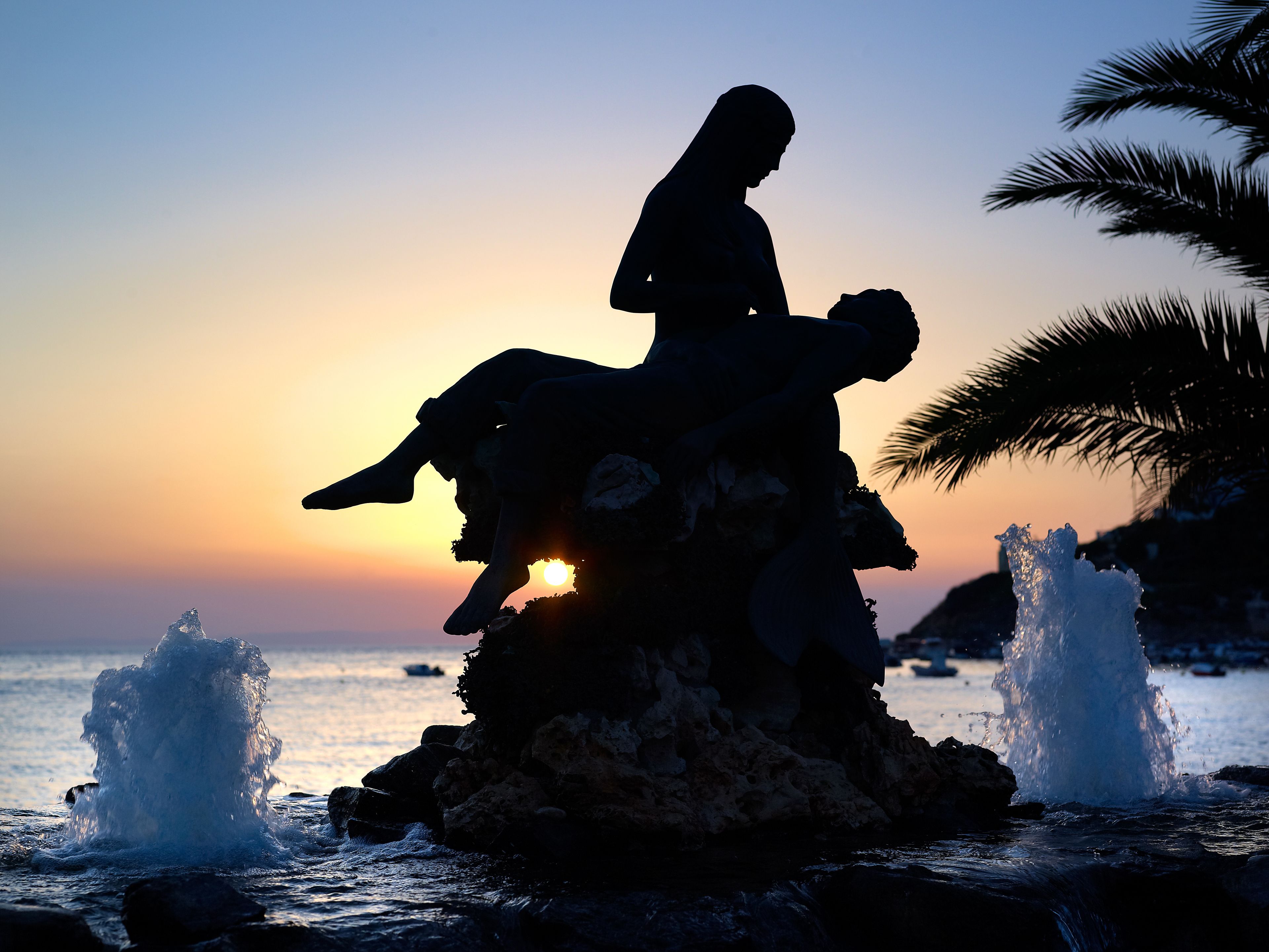 A silhouette of a person sitting on a rock by the sea at sunset.