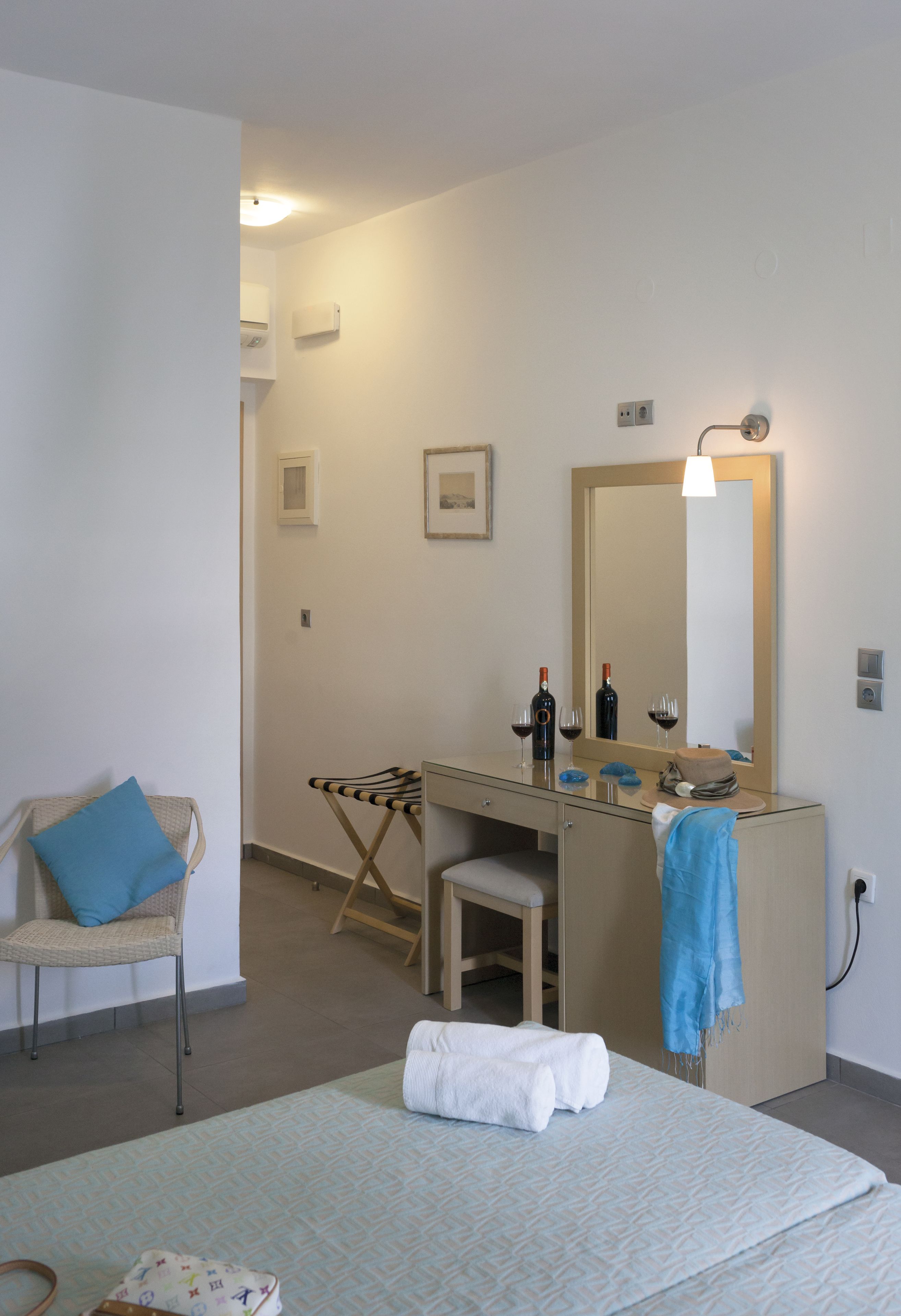 A hotel room with a bed, a chair, a desk with a mirror, and a small ironing board.