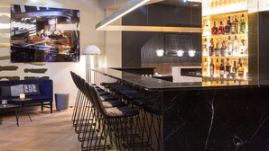 A modern bar area with a marble countertop, bar stools, and a wall-mounted TV. - THE FRITZ Düsseldorf (Düsseldorf)