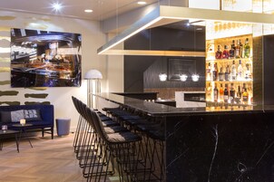 Zona de bar moderna con mostrador de mármol, taburetes y televisor montado en la pared.