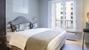 A bedroom with a bed, a nightstand, a window, and a door. - THE FRITZ Düsseldorf (Düsseldorf)