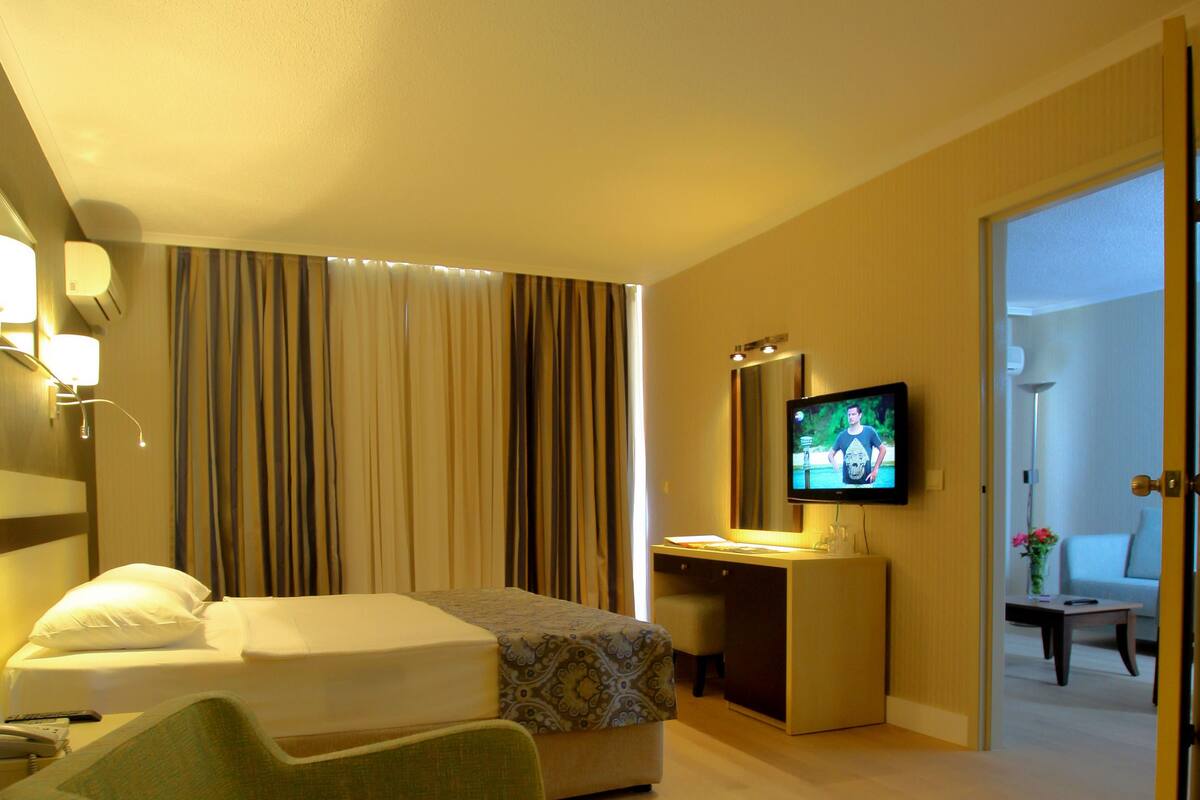 A hotel room with a bed, a desk with a TV, a chair, and a small table with a tray.