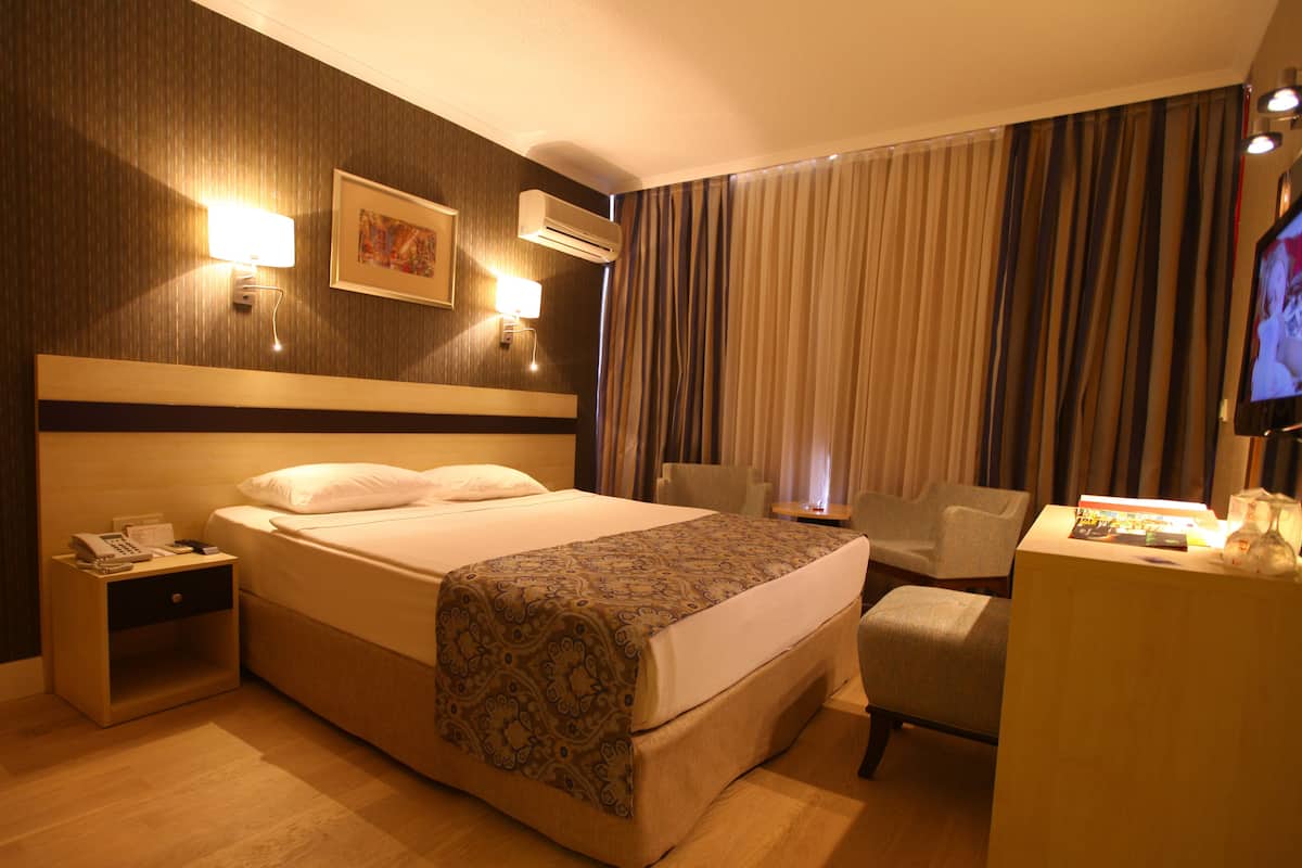 A hotel room with a large bed, bedside tables, a desk, a chair, and a television.