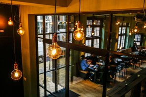 A restaurant with hanging light bulbs, large windows, and a wooden interior. - Vesting Hotel Naarden (Naarden)