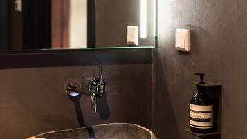A stone sink with a modern faucet, a mirror, and a wall-mounted soap dispenser in a bathroom.