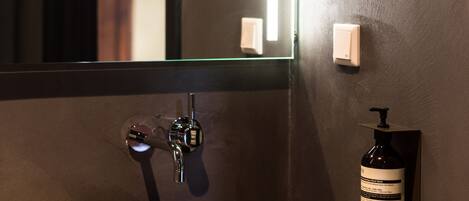 A stone sink with a modern faucet, a mirror, and a wall-mounted soap dispenser in a bathroom.