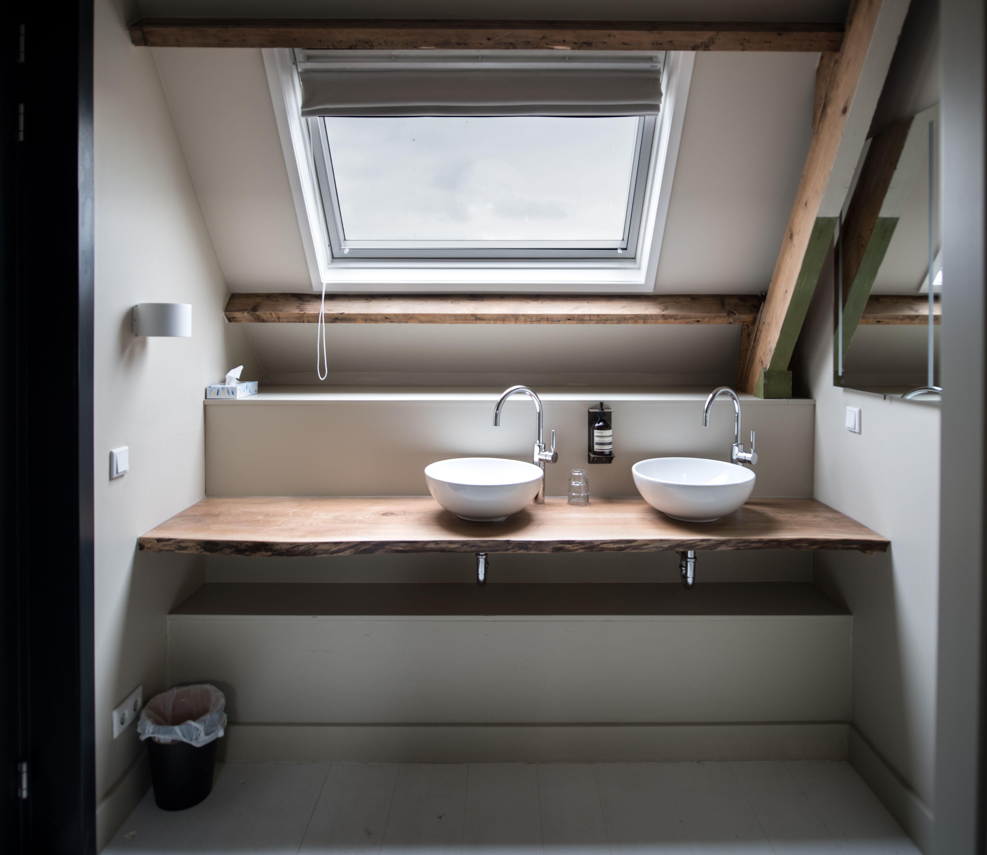 Een badkamer met twee wasbakken, een dakraam en houten balken.