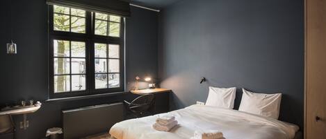 A bedroom with a large window, a desk, and a bed with towels.