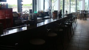 A bar area with a long counter, multiple chairs, and a view of greenery outside.