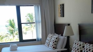 A hotel room with two beds, a TV, a lamp, and a window with curtains.