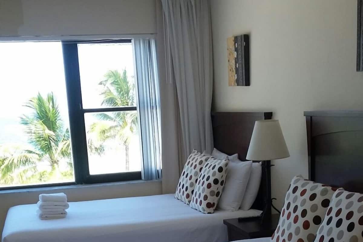 A hotel room with two beds, a TV, a lamp, and a window with curtains.