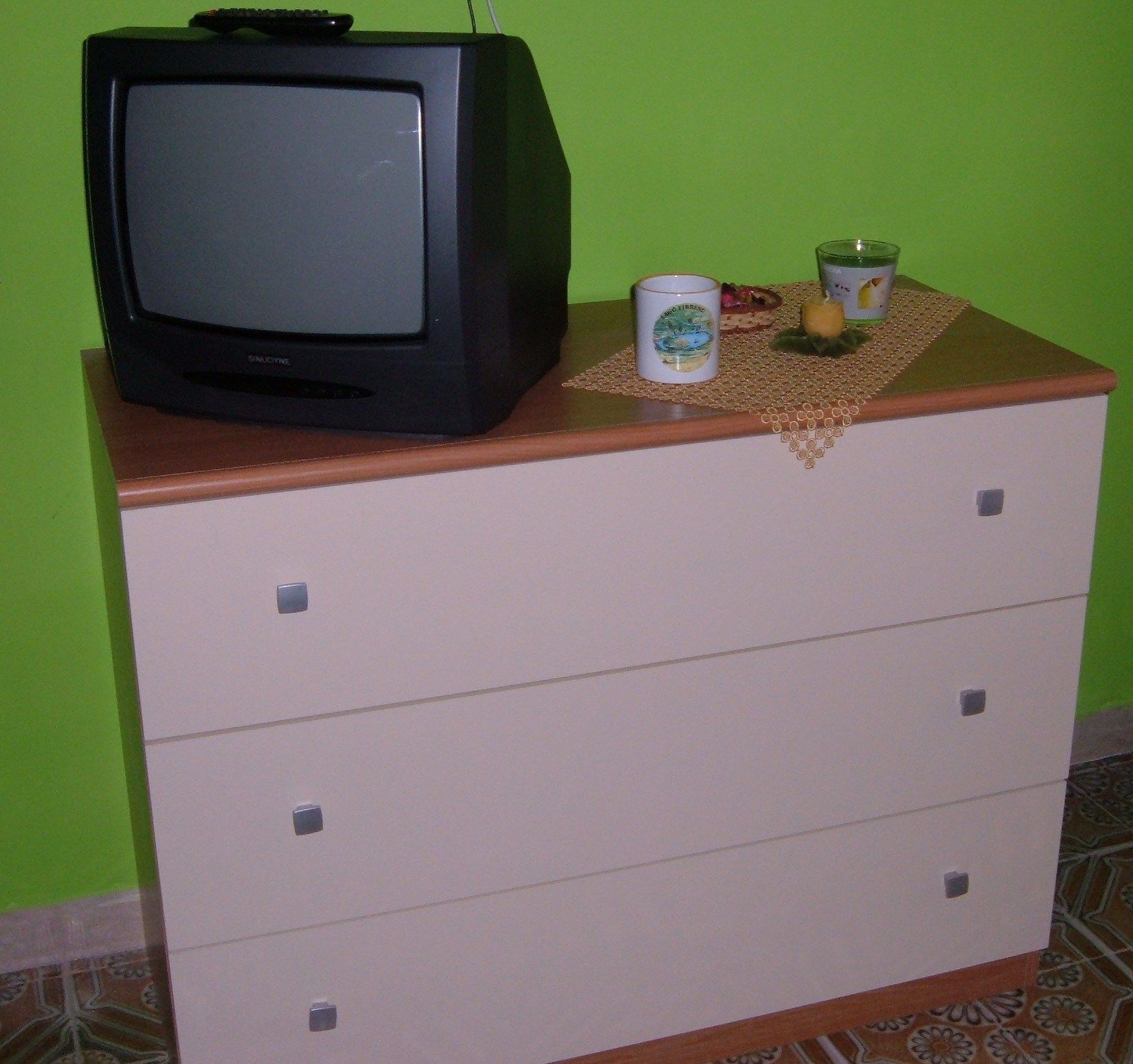 Un televisore su una cassettiera con cassetti, una candela e un piccolo oggetto decorativo.