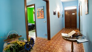 Un pasillo con paredes azules, piso estampado, una puerta de madera y una mesa con papeles y una cesta de flores.