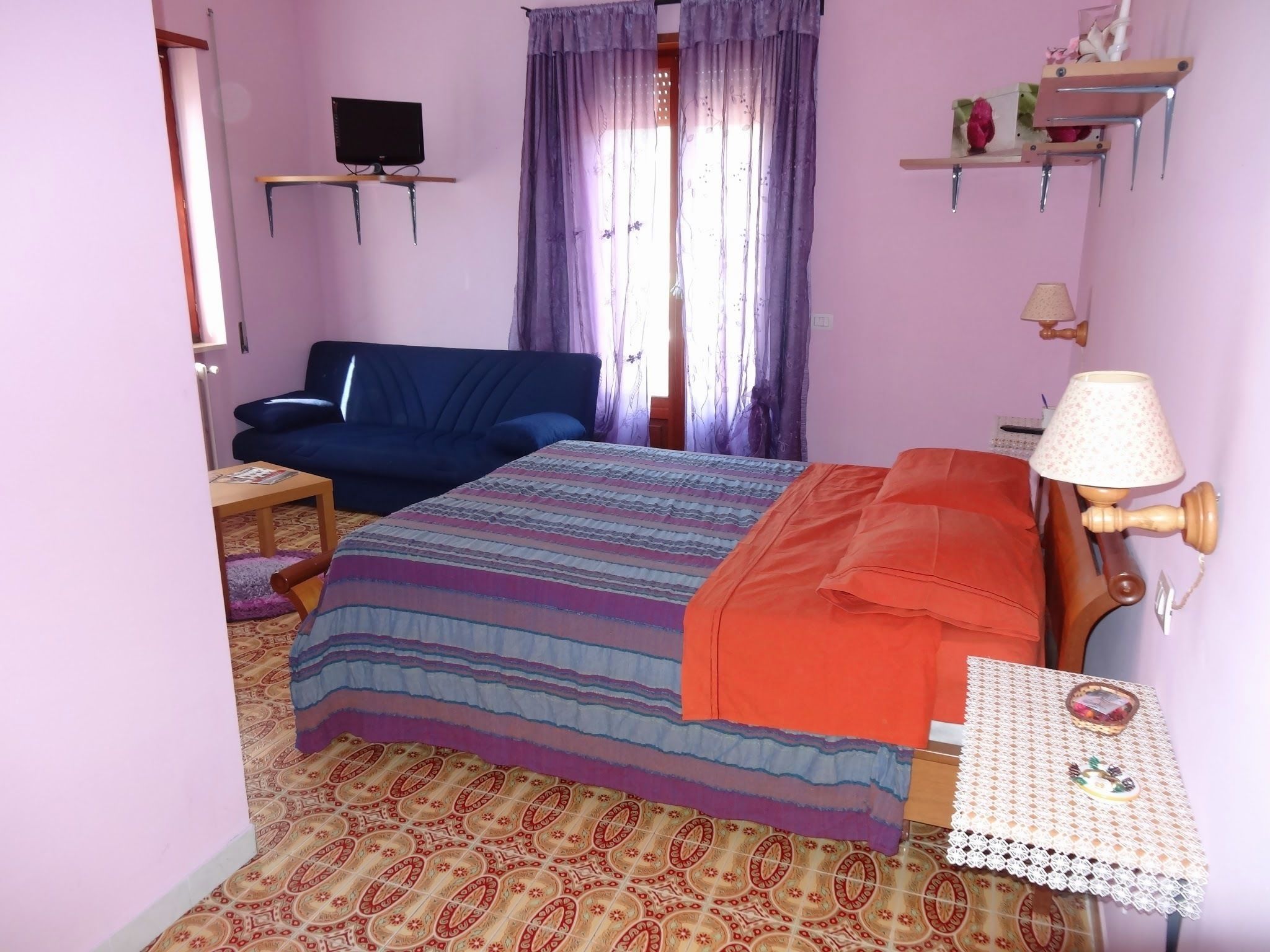 Une chambre à coucher avec un lit, un téléviseur posé sur un meuble, un bureau, une chaise et une fenêtre avec des rideaux.