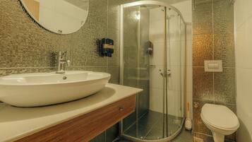 Een badkamer met een rond wastafel, een douchecabine van glas en een toilet.